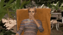 a woman in a striped sweater is sitting on a chair drinking a drink
