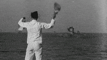 a black and white photo of a man standing in the ocean waving his hat