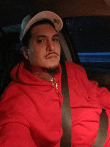 a man wearing a red hoodie and a white hat is in a car