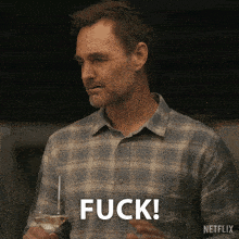 a man in a plaid shirt is holding a glass of wine and saying " fuck "