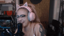 a woman wearing headphones and glasses is laughing into a microphone .