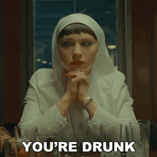 a nun is sitting at a table with glasses and the words you 're drunk below her