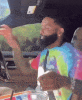 a man in a tie dye shirt is sitting in a car with his arms outstretched