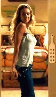 a woman in a white tank top is standing in front of a bedroom door with a paddle on it
