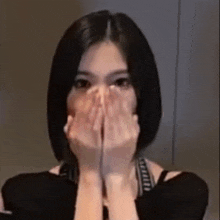 a woman is covering her face with her hands and looking at the camera .