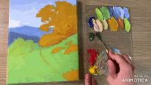 a person is painting a landscape on a canvas with a palette of paints in the background