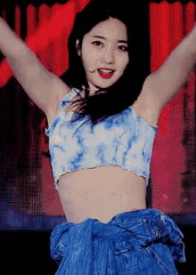 a woman in a blue tie dye crop top and blue jeans is dancing with her arms outstretched