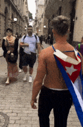 a man with a cuban flag on his back walks down a brick street