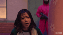 a girl in a green and white shirt is standing in front of a man in a pink suit with a netflix logo on it