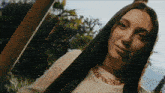 a woman with long dark hair wearing a white shirt and a gold chain around her neck