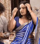 a woman in a blue striped saree is sitting on a bed next to a man .