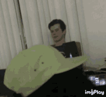 a man is sitting on a couch with a laptop and a green hat on his head .