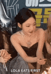 a woman in a black dress and pearls is sitting next to a group of women .