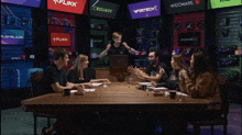 a group of people sitting around a table with a man standing in front of a laptop that says flikk on the screen