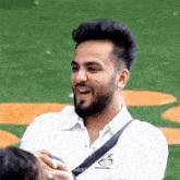 a man with a beard is wearing a white shirt and a black sling bag .