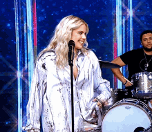 a woman singing into a microphone with a man playing drums in the background