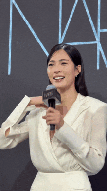 a woman in a white suit is holding a microphone with nars on it