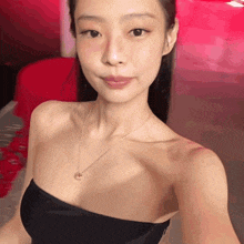 a woman wearing a black strapless top and a gold necklace takes a selfie