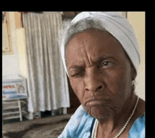 an elderly woman wearing a turban and a pearl necklace looks at the camera with her eyes closed
