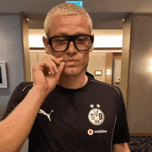 a man wearing glasses and a bvb shirt talks on a cell phone