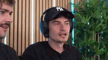 a man wearing headphones and a hat is talking to another man in a room .