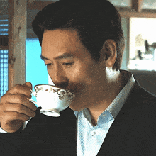a man in a suit is drinking from a teacup