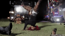 a woman with red hair is doing a handstand in front of a truck at night .