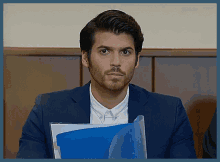 a man in a suit holds a blue folder in his hand
