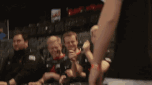 a group of men are sitting in a stadium and one of them is wearing a black shirt with the letter a on it