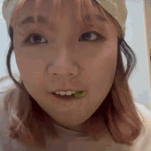 a woman with pink hair is eating a green leaf