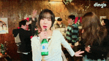 a woman is holding a bottle of beer in front of a group of people and the word dingo is on the bottom