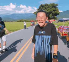 a man wearing a monster t-shirt is standing on a road
