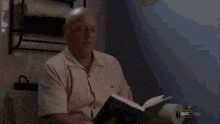 a bald man is reading a book while sitting in a room .