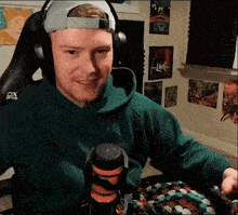 a man wearing headphones and a green hoodie is sitting in front of a microphone that says dx on it