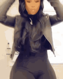 a woman wearing a leather jacket and black pants is dancing in front of a window .