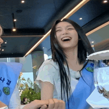 a woman laughs while wearing a blue apron that says ' n.k. ' on it
