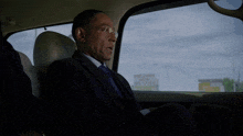 a man in a suit and tie sits in the back seat of a car and says can i see it