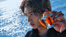 a man is holding a toy in his hand in front of the ocean