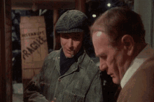 a man is talking to another man in front of a sign that says fragile