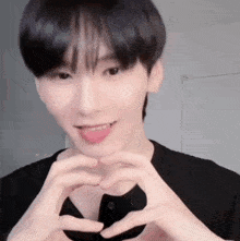 a young man is making a heart shape with his hands and sticking out his tongue .