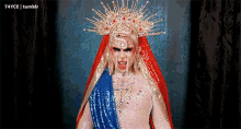 a drag queen with a crown on her head and a blue and red robe