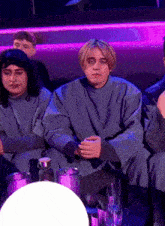 a group of people are sitting in a dark room with a purple light behind them