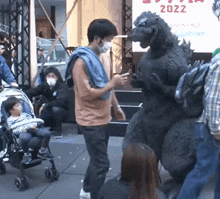 a man in a mask is standing next to a statue of godzilla .