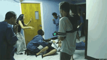 a group of people are standing around a woman laying on the floor while a man holds a camera in front of a door
