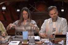 a man and a woman sit at a table with a man wearing a shirt that says " rest con "