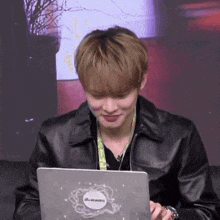 a man wearing a black leather jacket is using a laptop with a sticker on it that says lenovo