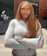a woman with long red hair is standing with her arms crossed in front of a building with a tiktok watermark on the bottom right