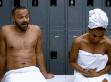 a man and a woman wrapped in towels are sitting on a bench in a locker room