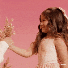 a little girl in a pink dress is being handed flowers by a man .