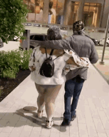 a man and a woman are walking down a sidewalk and the woman has a backpack on her back